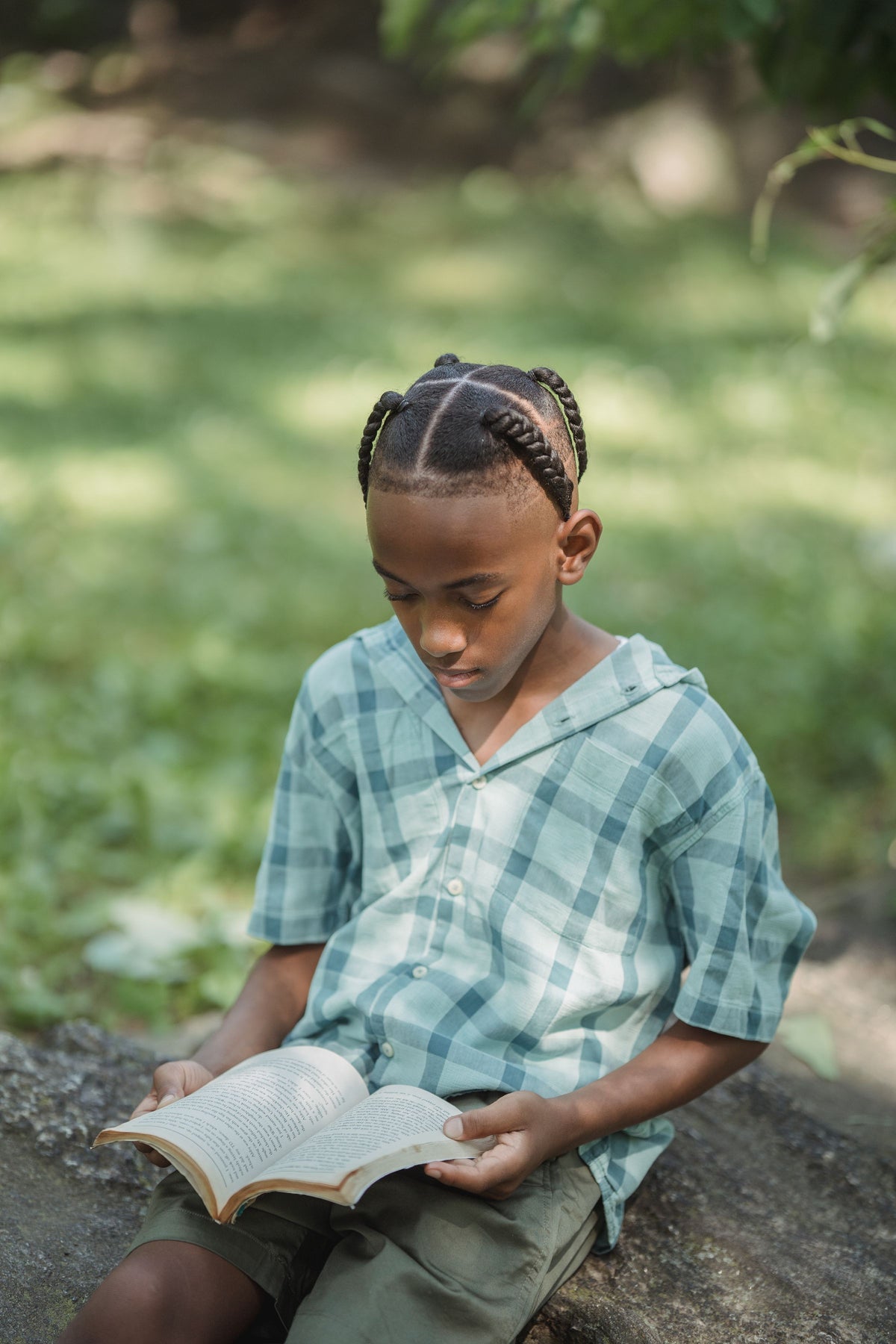 A boy reading a book outdoors on a fallen tree